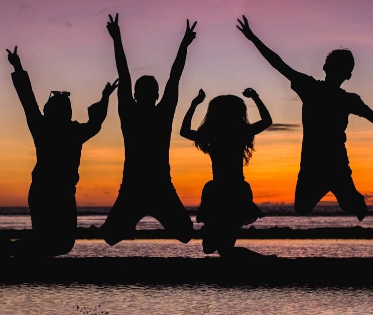 Silhouette of friends jumping on the beach at sunset, celebrating summer fun.